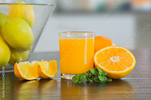 Glass of freshly squeezed orange juice with bowl of fruits on the background.