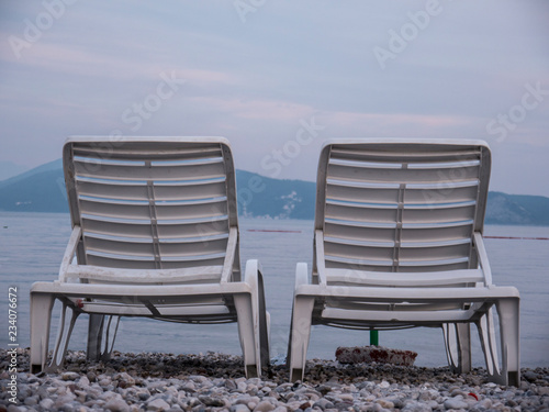 Two empty plastic chaise lounge on sea side at the end of season side view
