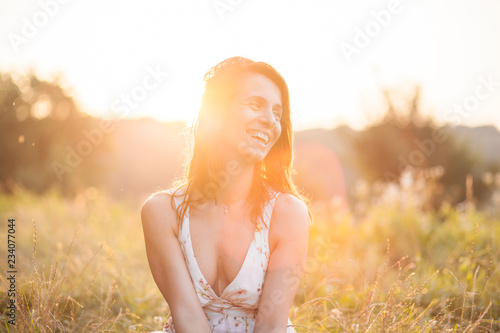 Beautiful brunette woman siting in the grass field during Sunset photo