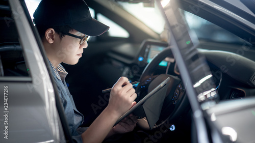 Fotografie Asian auto mechanic sitting on driver seat checking the car using digital tablet in auto service garage