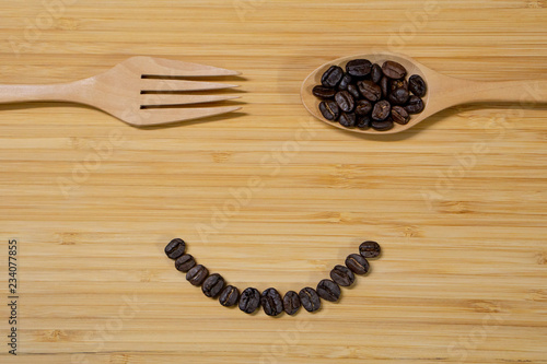 Smile face of coffee beans, wooden spoon and fork on wood table background. Top view. Happy eating concept