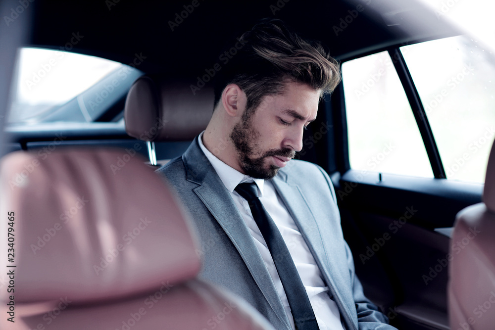 Unsmiling businessman sitting in the back seat in his car Unsmiling businessman sitting in the back seat in his car