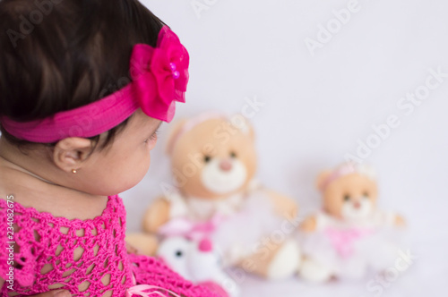 Baby with pink dress looking at the teddy bears blurred in the background