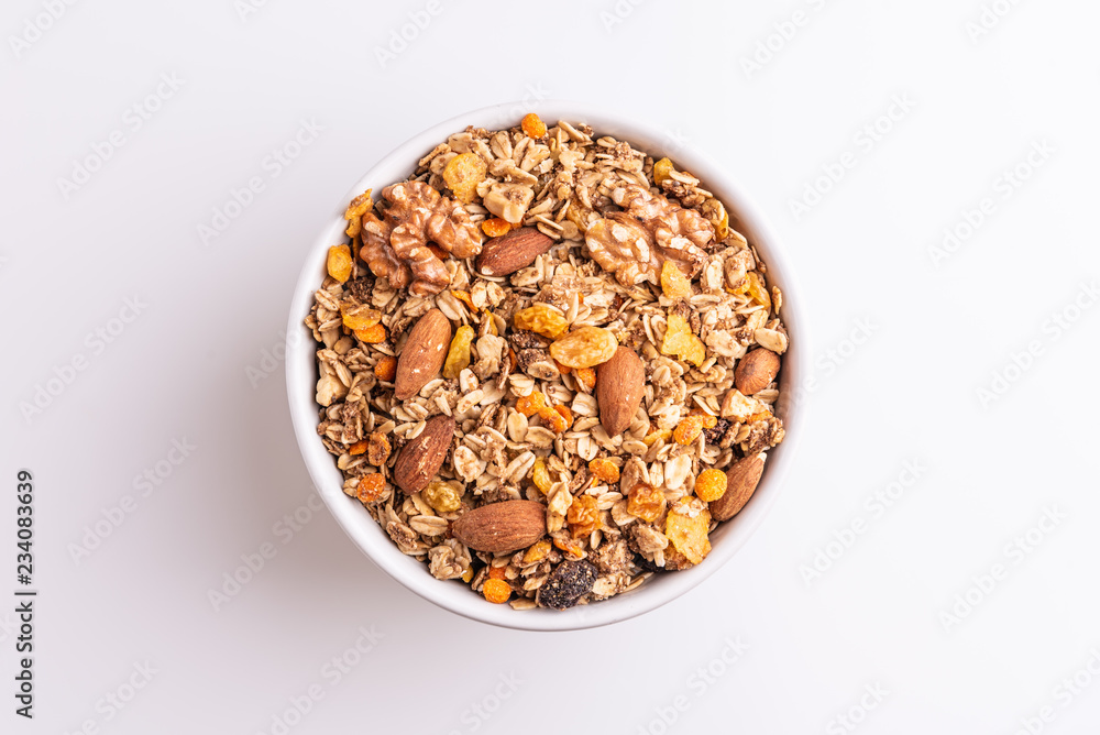 Granola or muesli with nuts and rasins in a white bowl on a white background, top view, soft light Granola or muesli with nuts and rasins in a white bowl on a white background, top view, soft light
