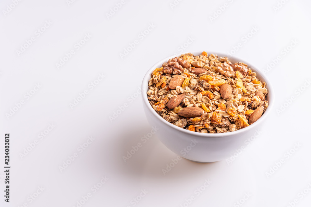 Granola or muesli with nuts and rasins in a white bowl on a white background, angle view, copy space, soft light Granola or muesli with nuts and rasins in a white bowl on a white background, angle view, copy space, soft light
