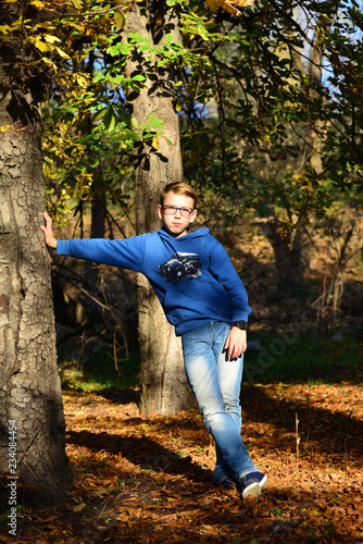 A boy standing near a tree in the forest on dry leaves on a summer evening, in nature.