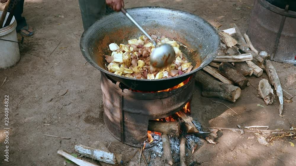 Stir-frying vegetables with pork in a wok on a large charcoal and wood brazier stove outdoors (upper view)