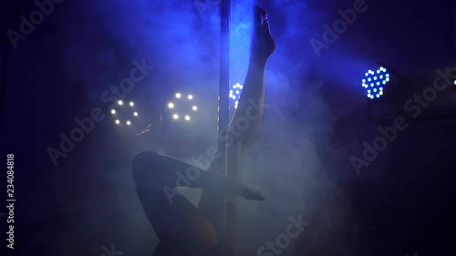 Silhouette of a sexy girl who does a complex exercise on a pylon in the dark. Slow motion.