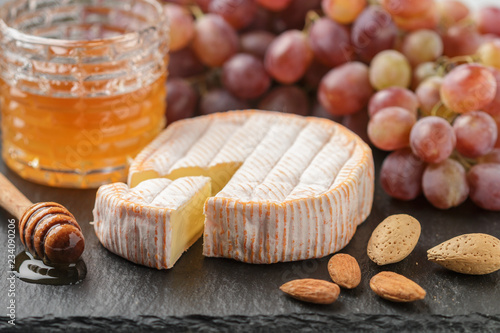 Delicatessen soft fragrant cheese with mold, honey, almonds and red grapes on a black slate plate. Snacks for gourmets