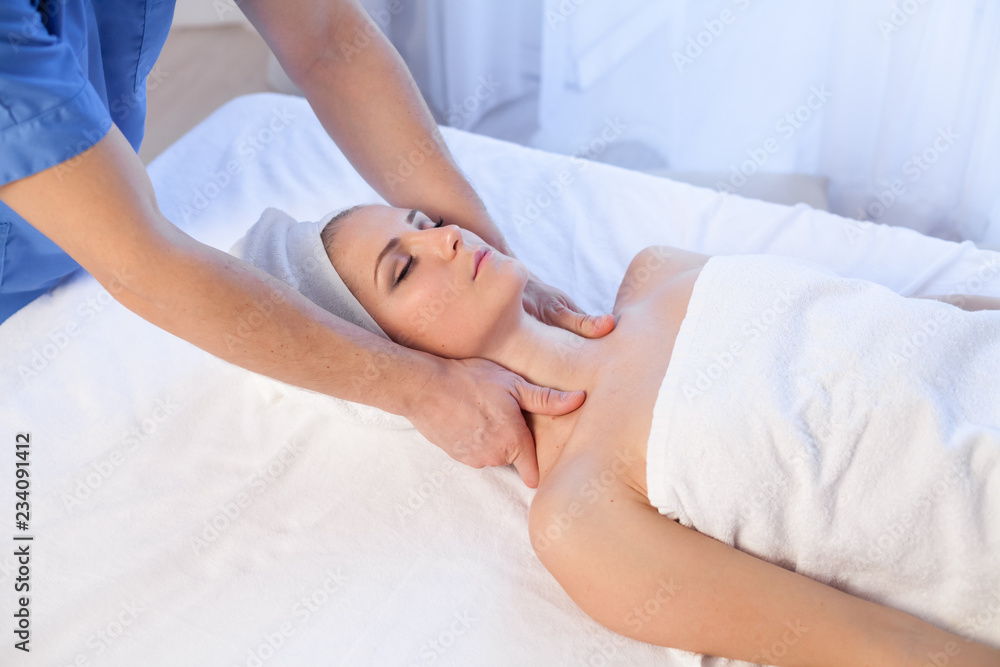 a massage therapist makes a woman face and neck massage in the Spa