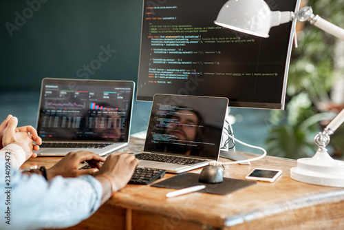 Programmers writing a program code sitting at the workplace with three monitors in the office. Cropped imaage with no face