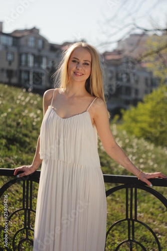 young blonde girl in a white semi-transparent dress in the sun