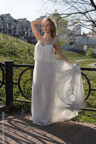 young blonde girl in a white semi-transparent dress in the sun