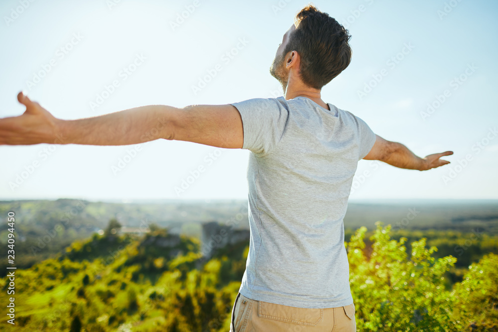 Man extending arms and admiring the view on sunny day Man extending arms and admiring the view on sunny day