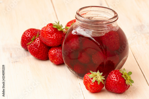 Strawberry jam in a jar with fresh strawberries on white wooden background. Glass jar with delicious strawberry confiture. Fresh homemade strawberry jam with berries in small jars, selective focus