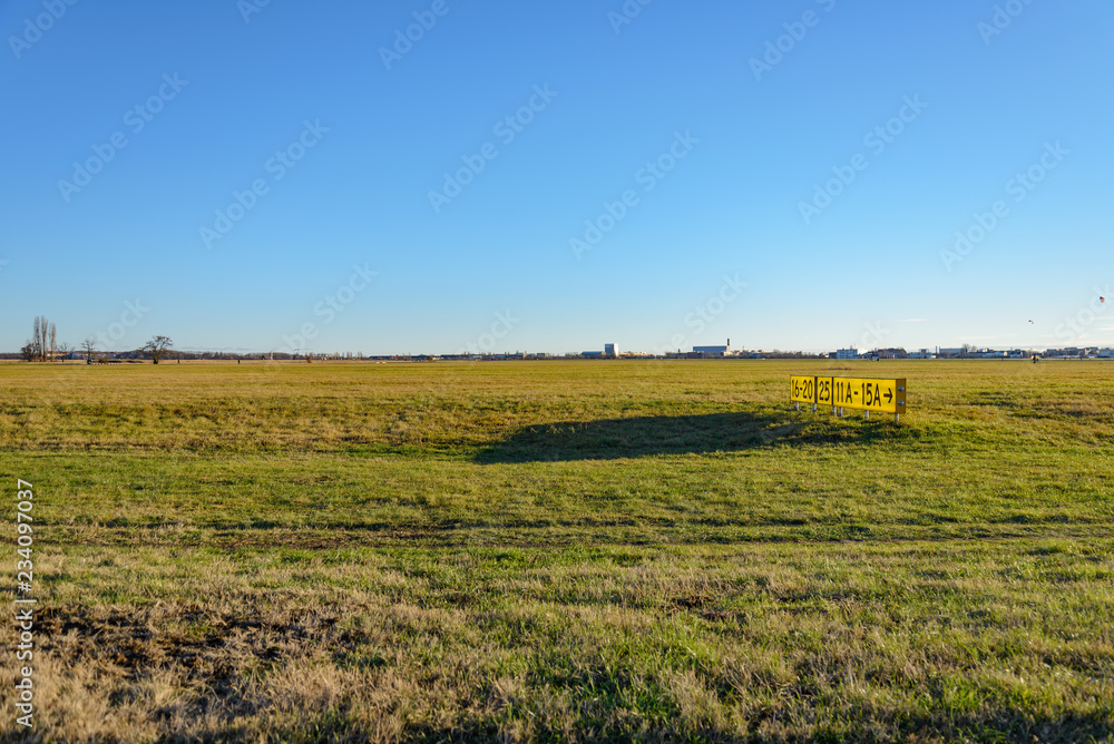 Horizontal landscape scenery of grass field and old yellow signal number on the former landing field of Tempelhof park, previous airport, in Berlin, Germany with clear sunny sky.
