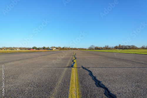 Fotografija Close up low angle diminish perspective view of cracking asphalt road, airport runway or airfield at Tempelhof Field park, former airport, with clear blue sunny sky in Berlin, Germany