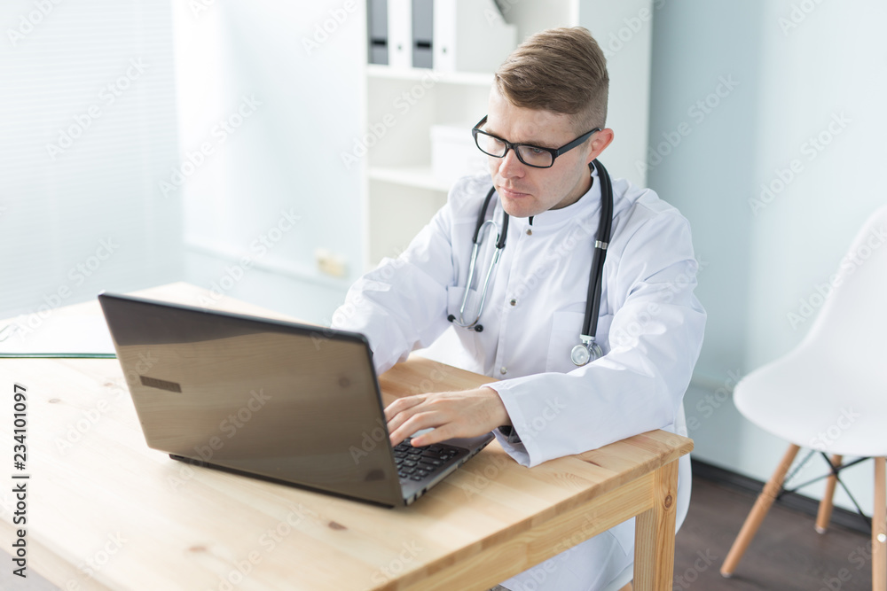 Medicine, working and people concept - doctor sitting at the table and working on laptop Medicine, working and people concept - doctor sitting at the table and working on laptop