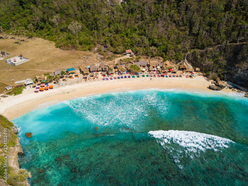 Aerial view to beautiful Atuh beach with buildings, sunbeds and hindu temple. Turquoise ocean water. Photo from drone. Nusa Penida, Bali, Indonesia