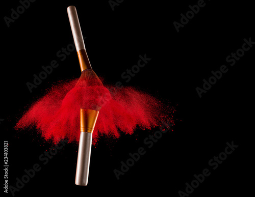 Makeup brush with red powder explosion on black background