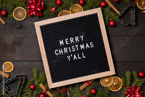 Merry  Christmas Y' all letter board on dark rustic wood background with Christmas decoration and fir branch frame top view flatlay