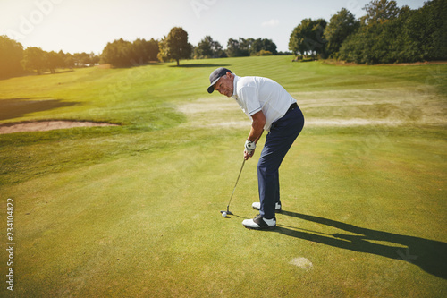 Bilde på lerret Senior man preparing to putt on a golf course green