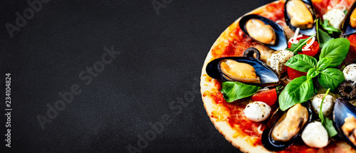 Seafood Italian Pizza on black stone background, top view. Pizza with Mussels, Tomatoes, Basil leaf and Mozzarella Cheese close up. Copy space
