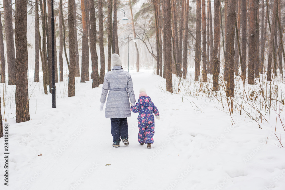 Winter, family and people concept - Mother is walking with her little daughter in snowy park, back view
