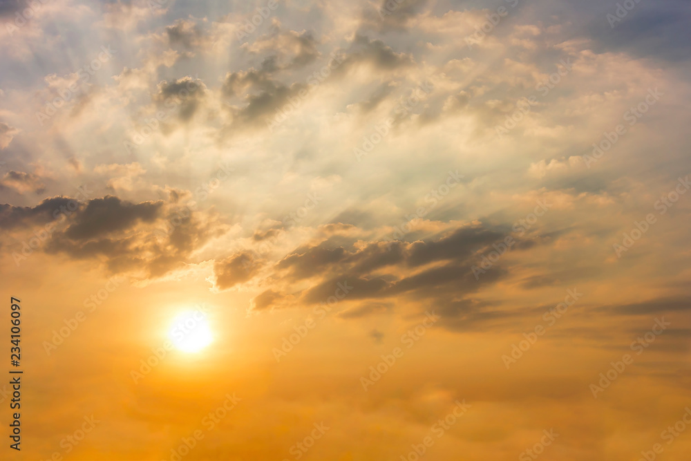 Fototapeta premium Sunset in the twilight time with Clouds and sun shines through rays of light sky yellow and orange color in the illuminated picturesque sky over the trees.