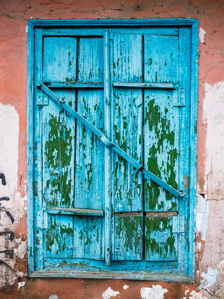 Naklejka premium Old blue closed window with shutters. Ruined wall of an old house