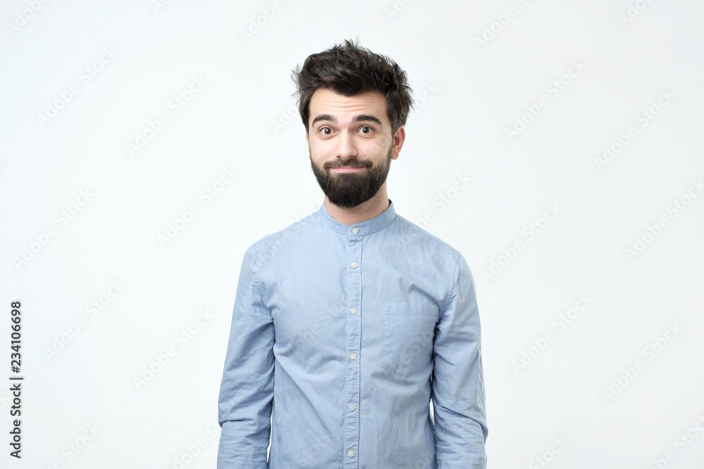 Tired hispanic man in blue shirt with beard looking confusedly at camera Tired hispanic man in blue shirt with beard looking confusedly at camera