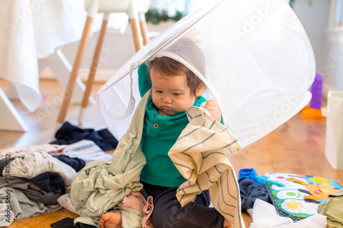Toddler boy playing with laundry in a laundry basket