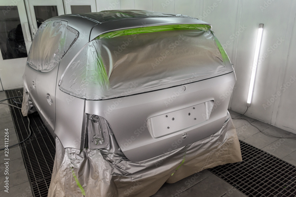 Full painting of the car in the back of a silver hatchback window and the wheels of which are covered with paper from hitting the paint in a special camera for body repair of vehicles in the workshop Full painting of the car in the back of a silver hatchback window and the wheels of which are covered with paper from hitting the paint in a special camera for body repair of vehicles in the workshop
