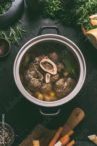 Foto Broth of beef meat shin with bone in cooking pot on dark kitchen table background with ingredients for soup, top view