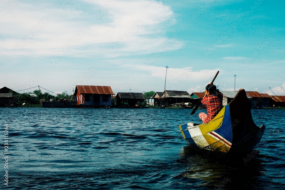 local woman crossing the lake on his canoe in front of the floating stilt house settlement
