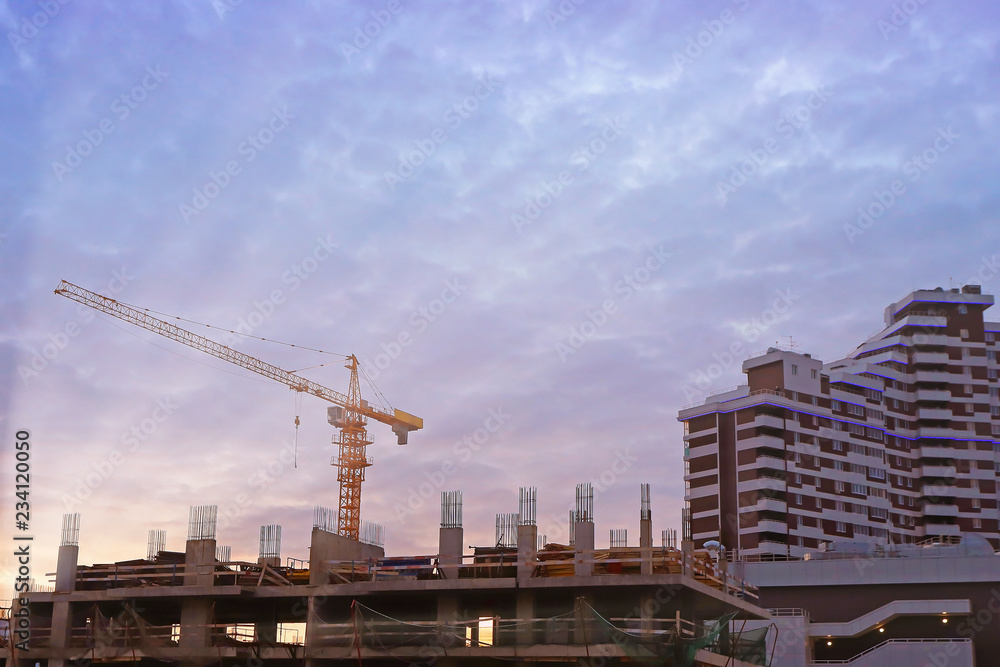 construction of high-rise buildings with yellow tower crane at sunset and dark blue clouds
