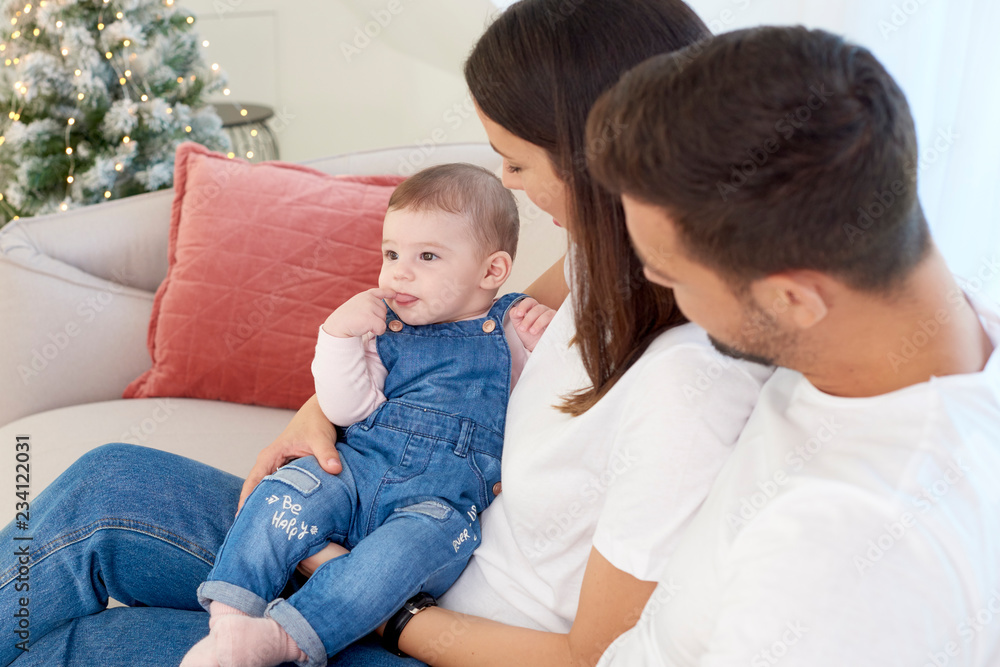 Happy young parents with their baby girl enjoy Christmas time while relaxing on the sofa Happy young parents with their baby girl enjoy Christmas time while relaxing on the sofa