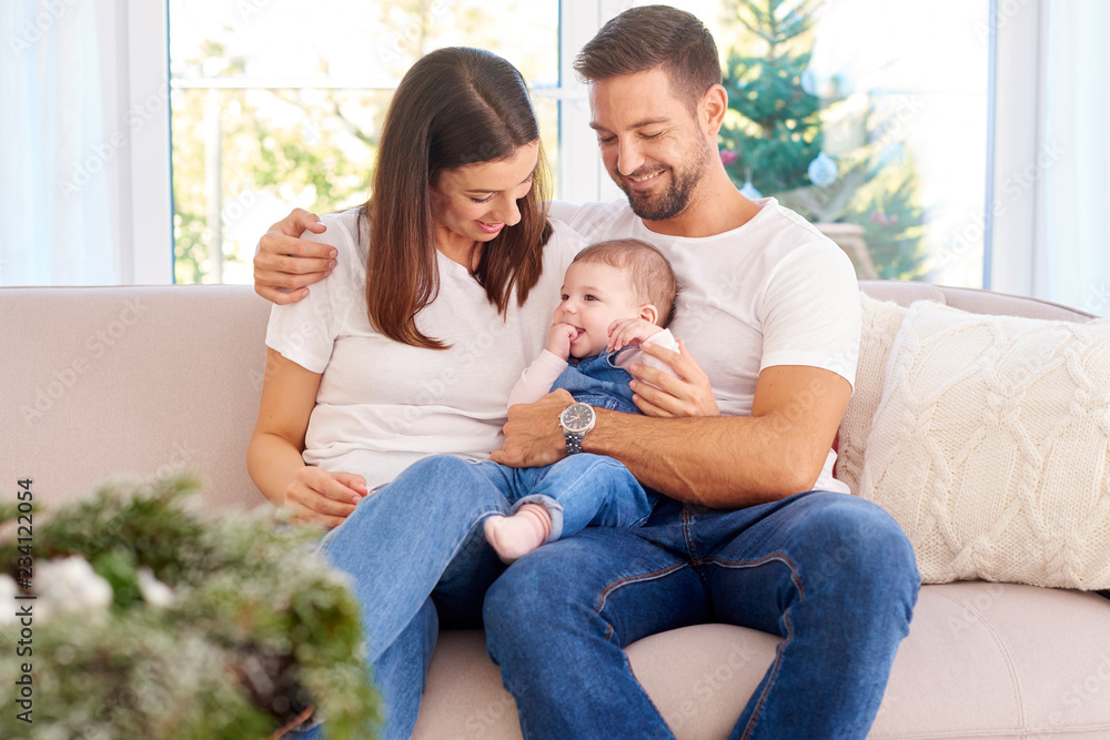 Happy young parents with their baby girl enjoy Christmas time while relaxing on the sofa Happy young parents with their baby girl enjoy Christmas time while relaxing on the sofa