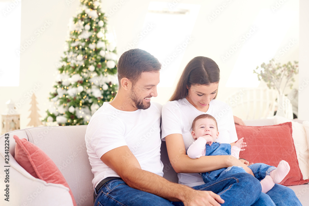 Happy young parents with their baby girl enjoy Christmas time while relaxing on the sofa. Family life. Happy young parents with their baby girl enjoy Christmas time while relaxing on the sofa. Family life.