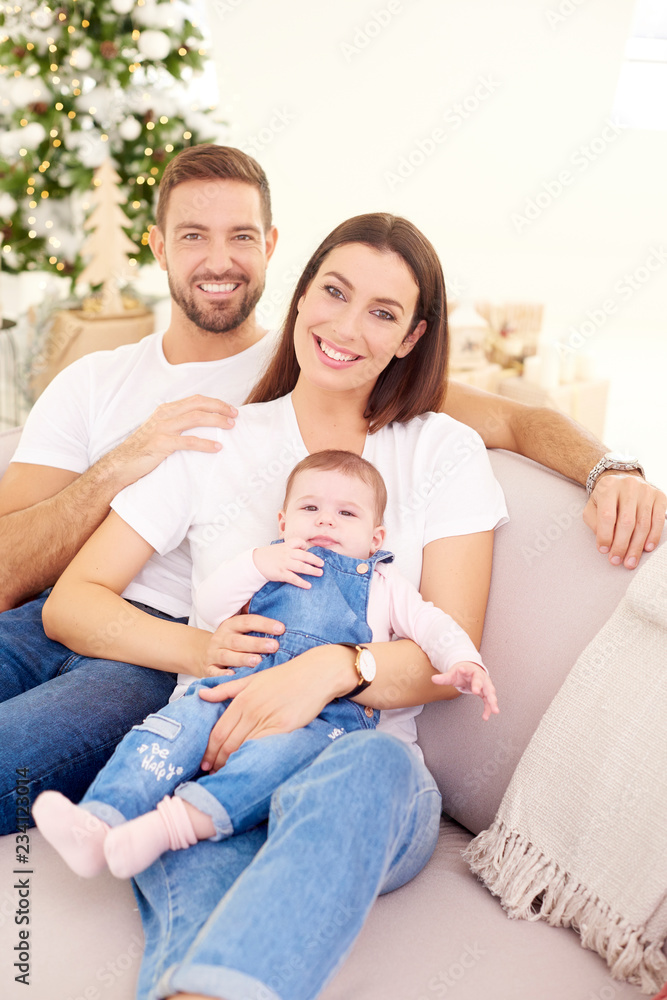 Happy young parents with their baby girl enjoy Christmas time while relaxing on the sofa Happy young parents with their baby girl enjoy Christmas time while relaxing on the sofa