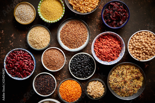 Various superfoods in smal bowls on dark rusty background. Superfood as rice, lentil, beans, peas, goji, flaxseed, buckwheat, couscous, chickpeas Top view Flat lay photo