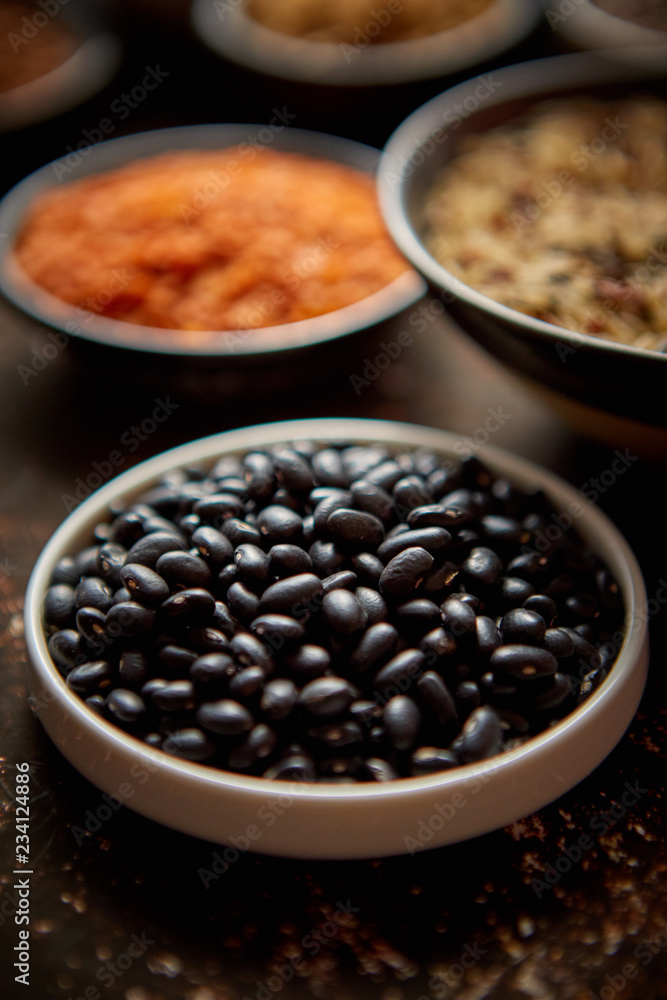Raw black beans in ceramic bowl. Composition of superfoods in background. Placed on dark rusty table. Selective focus. Raw black beans in ceramic bowl. Composition of superfoods in background. Placed on dark rusty table. Selective focus.