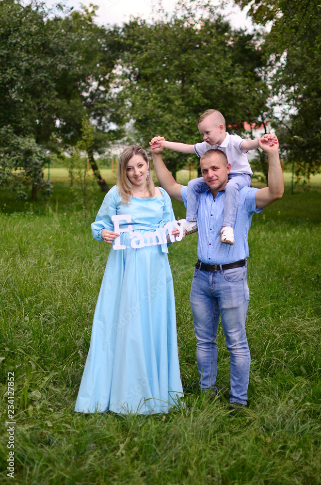 Naklejka premium Happy family together in summer garden/park. Mother holding inscription `family` .Father giving piggyback ride to son. Outdoor photo