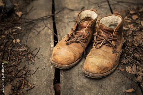 A pair of nubuck hiking boots on wooden floor with dead leaves ang twigs.