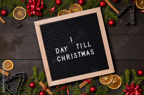 One Day till  Christmas  countdown letter board on dark rustic wood background with Christmas decoration and fir branch frame top view flatlay