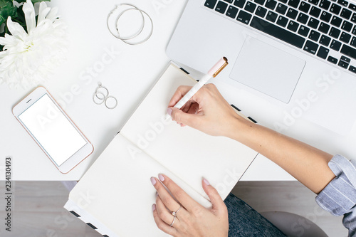 Female hands write in notebook on a white table with a keyboard and blank screen phone