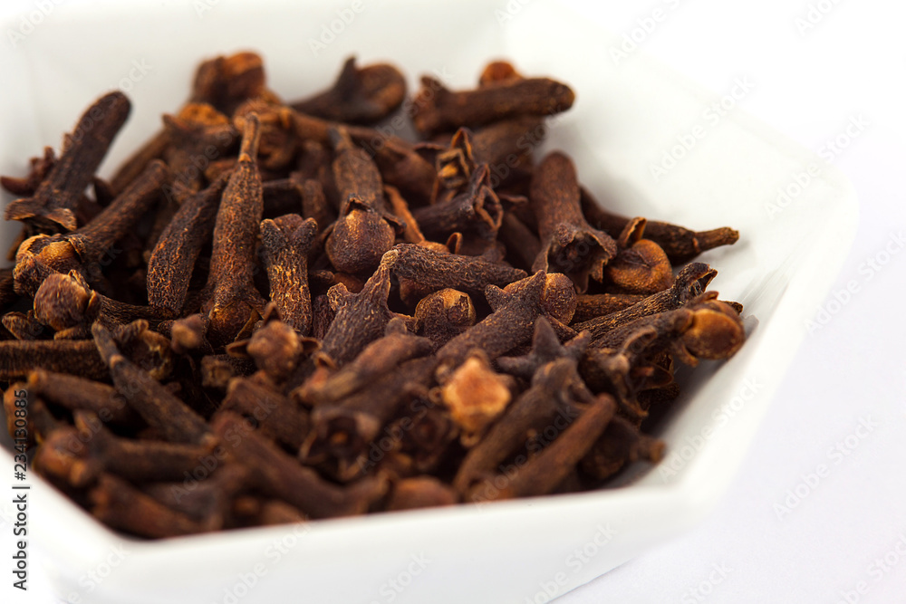 Fototapeta premium Spice cloves in a small white ceramic dish isolated on white background