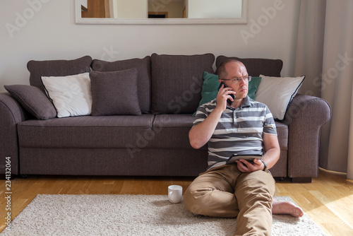 man sits on the floor near the sofa and talking on mobile phone photo