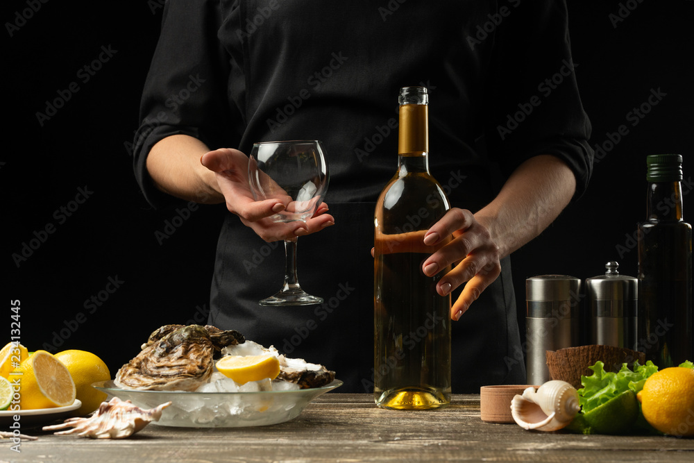 Chef pours, tastes Italian dry wine with oysters with lemon on a black background, the concept of seafood, wine, menus, recipes, restaurant and hotel