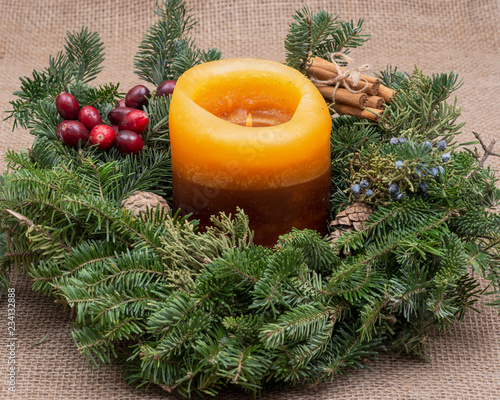 Winter holiday decoration: fraser fir table wreath centerpiece with cones, juniper, burning candle, cinnamon sticks tied with jute rope and cranberries on burlap background
